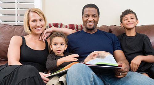 Smiling parent together with their two sons sitting on the sofa while browsing book photo